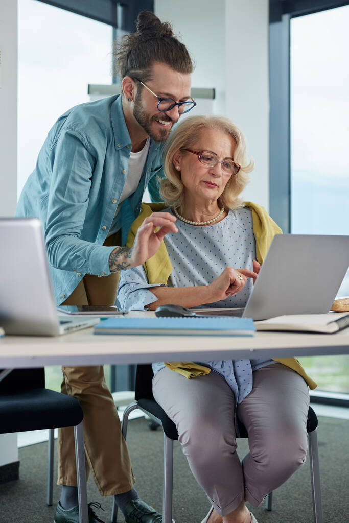 Man standing over an older woman showing her something on a computer